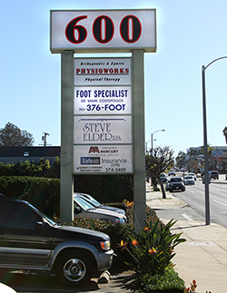 The image shows a sign with the name 600 prominently displayed, indicating a location likely related to medical services or physiotherapy, situated at an intersection with other businesses visible in the background.